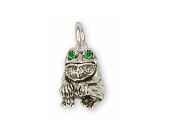 May include: A silver charm in the shape of a frog with green gemstone eyes. The frog is sitting with its legs crossed and has a detailed, realistic design.