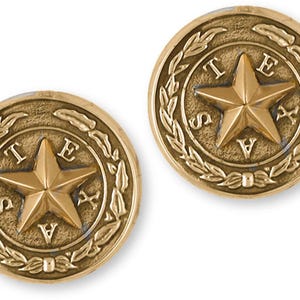 May include: A pair of gold-tone cufflinks featuring the state seal of Texas. The seal depicts a five-pointed star surrounded by a laurel wreath and the letters "TEXAS".