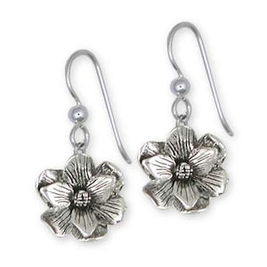 Puede incluir: Un par de pendientes plateados con forma de flor. Cada pendiente presenta un diseño de flor abierta y detallada con un centro texturizado y delicados pétalos. Los pendientes tienen un cierre de gancho con un pequeño adorno de bola.