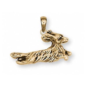May include: A gold-colored pendant in the shape of a running dog. The pendant has a detailed design, with visible fur and a loop at the top for a chain. The dog is in mid-stride, giving the impression of movement.