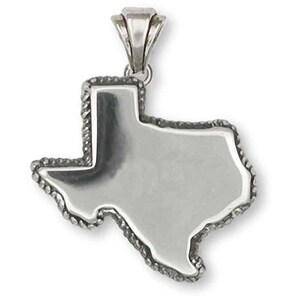 Puede incluir: Un colgante plateado con la forma del estado de Texas. El colgante tiene un borde en forma de cuerda y una argolla para una cadena. El colgante está hecho de un metal brillante y reflectante.