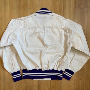 May include: White cotton bomber jacket with a blue and white striped collar and cuffs. The jacket has a ribbed waistband.