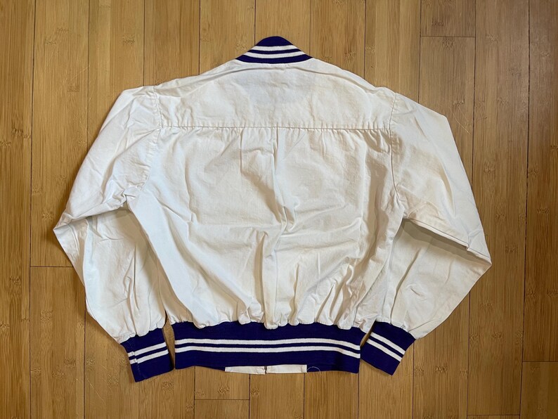 May include: White cotton bomber jacket with a blue and white striped collar and cuffs. The jacket has a ribbed waistband.