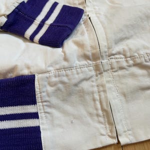 May include: White bomber jacket with purple and white striped cuffs. The jacket has a zip closure.