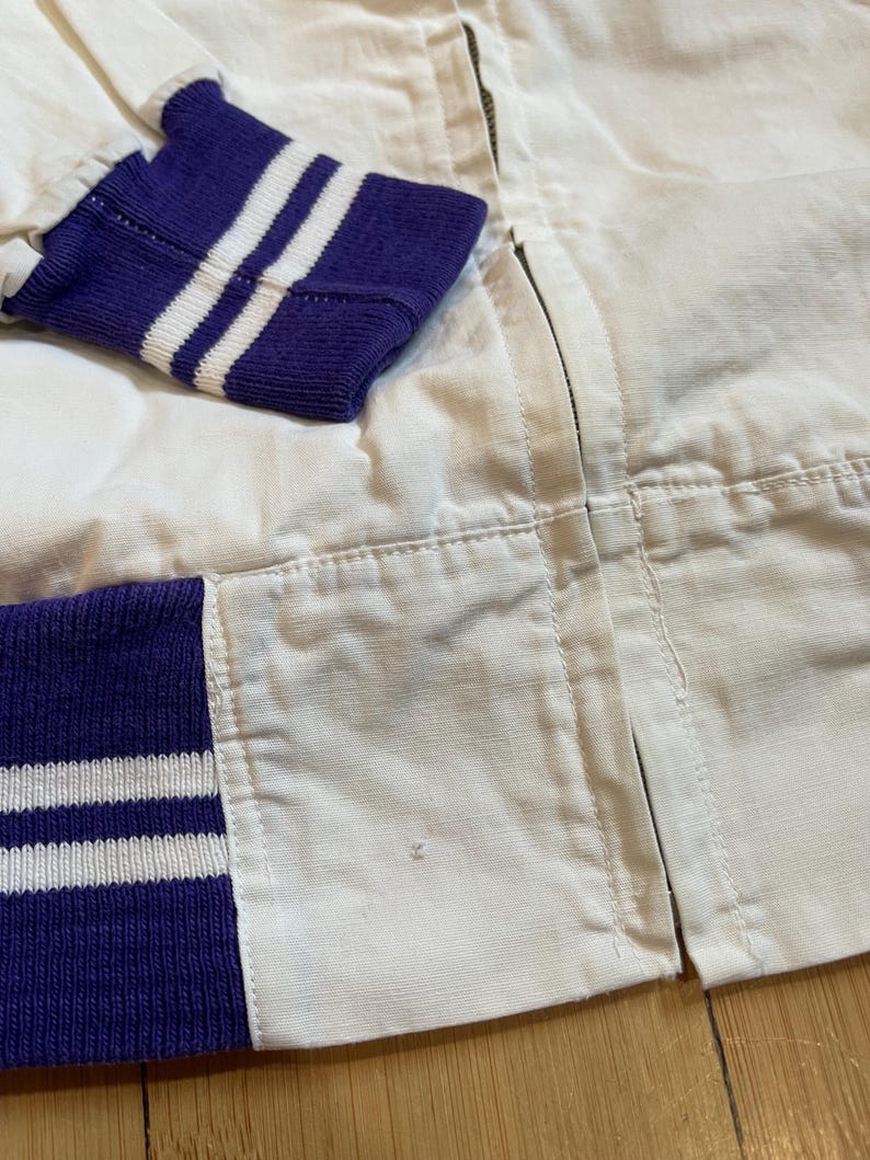 May include: White bomber jacket with purple and white striped cuffs. The jacket has a zip closure.