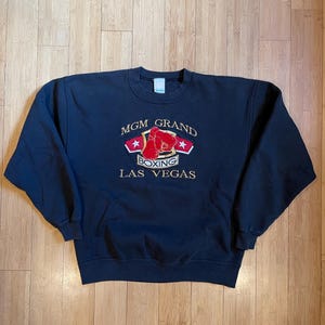 May include: Black sweatshirt with a gold embroidered logo that says "MGM Grand Boxing Las Vegas".