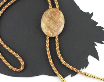 May include: A brown and tan braided bolo tie with a round, light brown and tan stone pendant.