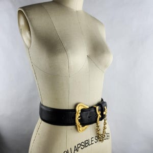 Puede incluir: Un cintur&oacute;n de cuero negro con una hebilla dorada grande y detalles de cadena. El cintur&oacute;n se muestra en un maniqu&iacute;. La hebilla tiene un dise&ntilde;o ornamentado. El cintur&oacute;n mide aproximadamente 5 cm de ancho.