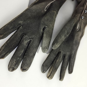 May include: A pair of black leather gloves with a worn look. The gloves have a long cuff and are fastened with buttons.