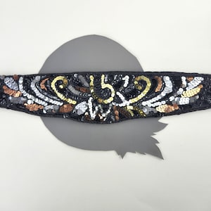 May include: Black sequined trim with gold and silver accents. The trim features a decorative design with a repeating pattern.