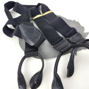 May include: Black suspenders with gold-tone clasps and leather detailing. These suspenders feature a classic design with adjustable straps and a textured finish. The leather accents add a touch of sophistication to the overall look.