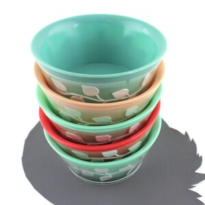 May include: A stack of four green bowls with a white leaf design. The bowls are nested inside each other, with the largest bowl on the bottom and the smallest bowl on top. The bowls are on a gray surface.