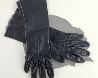 May include: A pair of black leather gloves with white stitching. The gloves are long and have a classic style.