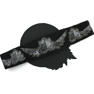 May include: A black beaded belt with silver floral embellishments. The belt is on a black background.