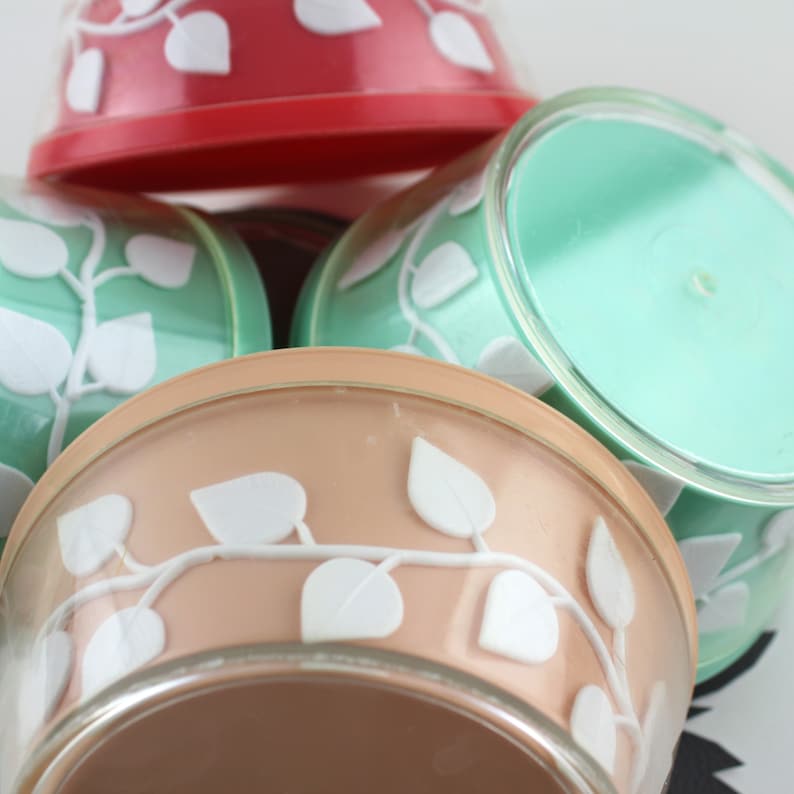 May include: Three vintage plastic containers with a white leaf design. The containers are red, green, and beige.