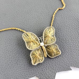May include: A gold-colored butterfly pendant necklace. The butterfly design features intricate wire detailing with a small pearl accent in the center. The necklace chain is also gold-colored, and the butterfly is set against a gray background.