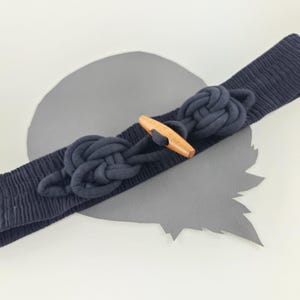 Puede incluir: Un cinturón de tela negro con un diseño anudado y un cierre de madera.