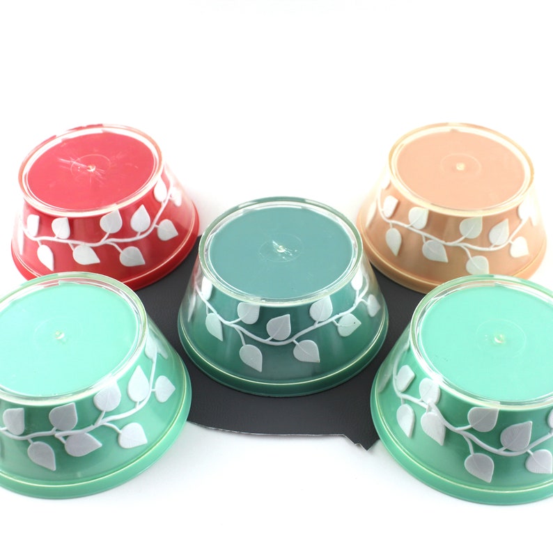May include: Five vintage plastic bowls with a white leaf design. The bowls are in various colors, including red, orange, and green.