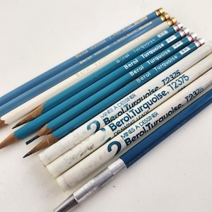 Może przedstawiać: Kolekcja niebieskich i białych ołówków z napisami "Berol Turquoise" i "Berol Verithin". Ołówki ułożone są na białej powierzchni, z widoczną srebrną temperówką. Ołówki mają różne odcienie niebieskiego.
