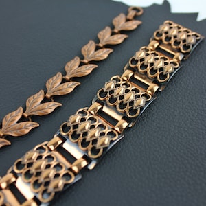 May include: Two copper bracelets with intricate designs. One bracelet features a repeating leaf pattern, while the other has a geometric, diamond-shaped design.