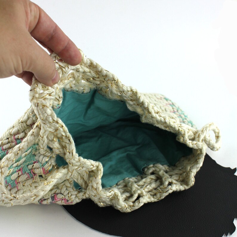 May include: A white crocheted drawstring bag with gold thread accents and a turquoise lining. The bag is open and the lining is visible.