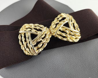May include: A dark brown elastic belt featuring a central gold-toned metal buckle. The buckle consists of two symmetrical, triangular-shaped components with a textured, rope-like twisted metal design and smooth, polished edges.