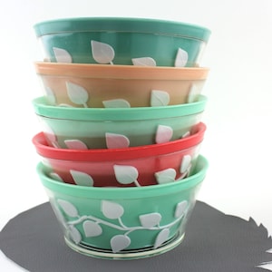 May include: A stack of five vintage plastic bowls with a leaf design. The bowls are in shades of green, peach, and red.
