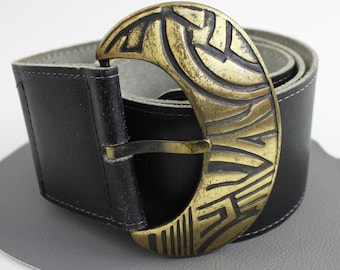 May include: A black leather belt with a large, gold-toned, crescent-shaped buckle. The buckle has a geometric design.