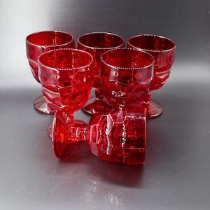 May include: Set of six red glass goblets with a textured, diamond-like pattern. The goblets are stacked and arranged on a dark grey surface.