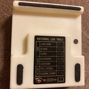 May include: A cream-colored plastic table stand with a black label that reads "RATIONAL LUX TABLE." The stand has a built-in measurement of 30 cm. It features a list of activities with corresponding measurements.