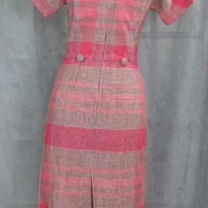 May include: A pink and beige plaid dress with short sleeves and a back zipper. The dress has two buttons at the waist.