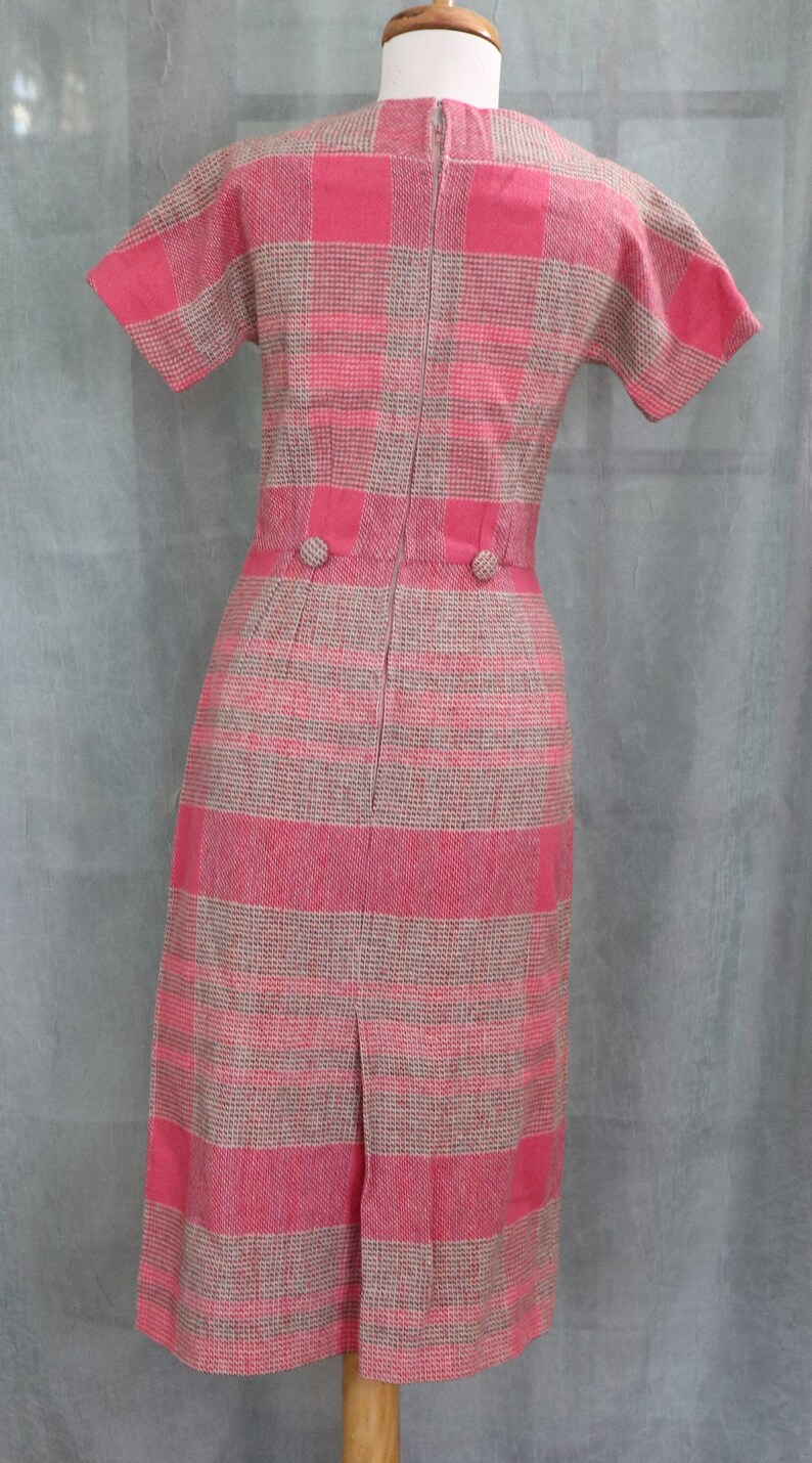 May include: A pink and beige plaid dress with short sleeves and a back zipper. The dress has two buttons at the waist.