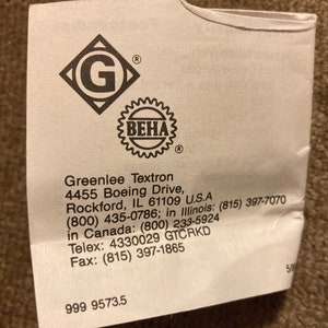 May include: A white paper label with the Greenlee Textron logo, a diamond with a 'G' inside, and a 'BEHA' seal. The label includes the company's address, phone numbers, and fax number. The number '999 9573.5' is printed at the bottom.