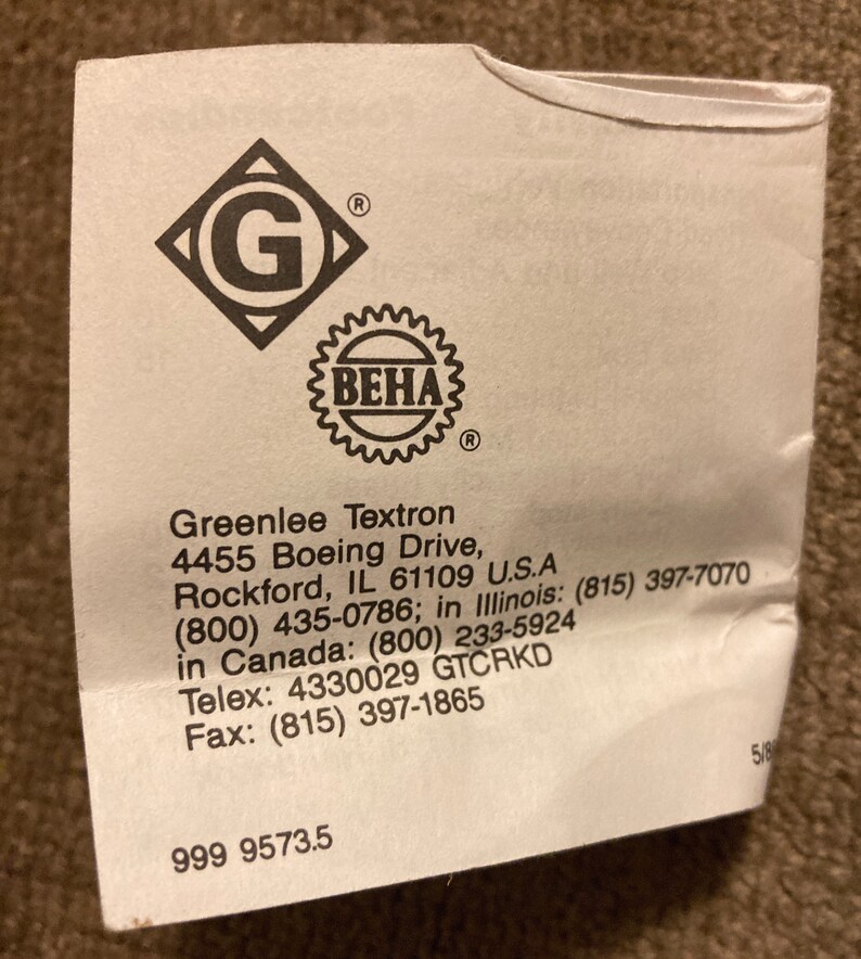 May include: A white paper label with the Greenlee Textron logo, a diamond with a 'G' inside, and a 'BEHA' seal. The label includes the company's address, phone numbers, and fax number. The number '999 9573.5' is printed at the bottom.
