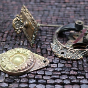 May include: Three antique brass doorbells with intricate floral designs. The doorbells are on a brown woven surface.