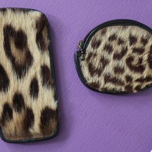 May include: Two small purses made of leopard print fur. The purses are both black with a brown and tan leopard print. One purse is rectangular and the other is a rounded oval shape.