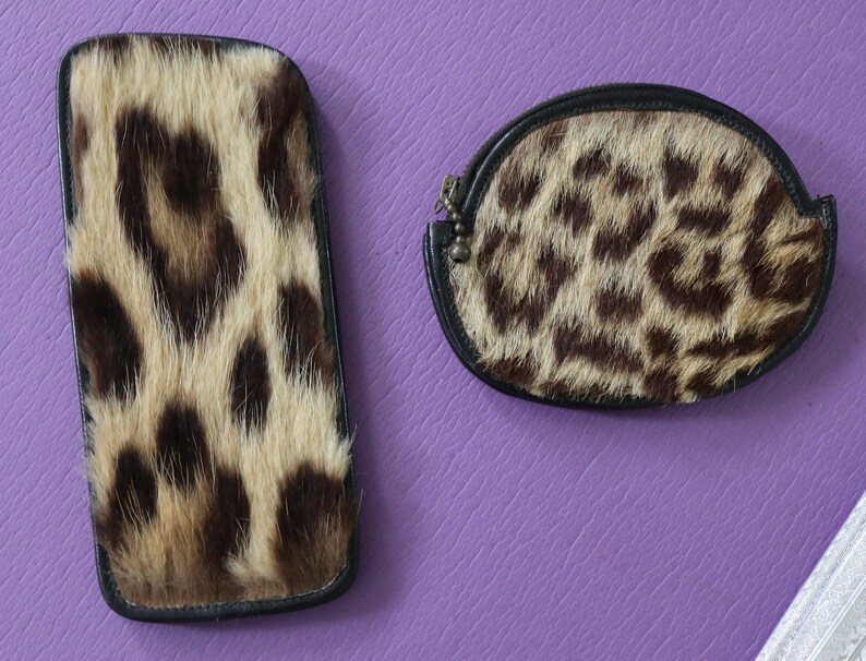 May include: Two small purses made of leopard print fur. The purses are both black with a brown and tan leopard print. One purse is rectangular and the other is a rounded oval shape.