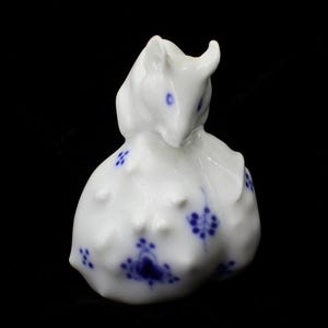 May include: A white porcelain figurine of a stylized animal, possibly a mouse or rat, with blue floral accents. The figurine has a rounded body and a detailed head with small ears and eyes. The blue floral pattern is repeated across the body.