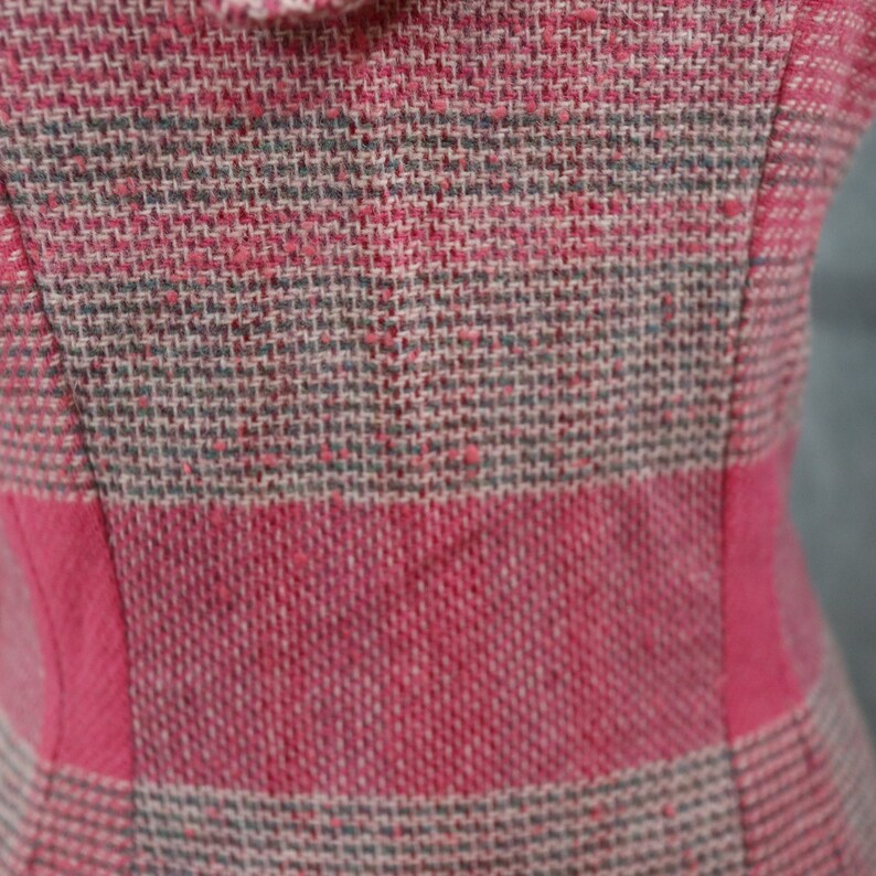 May include: Close-up of a pink and gray plaid fabric with a woven texture.