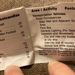 May include: A folded paper with text detailing lighting requirements for various areas and activities, including sports fields, playgrounds, and transportation vehicles. The text includes footcandle measurements.