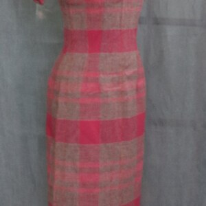 May include: A pink and brown plaid dress with short sleeves and a button closure at the neckline. The dress is on a mannequin.