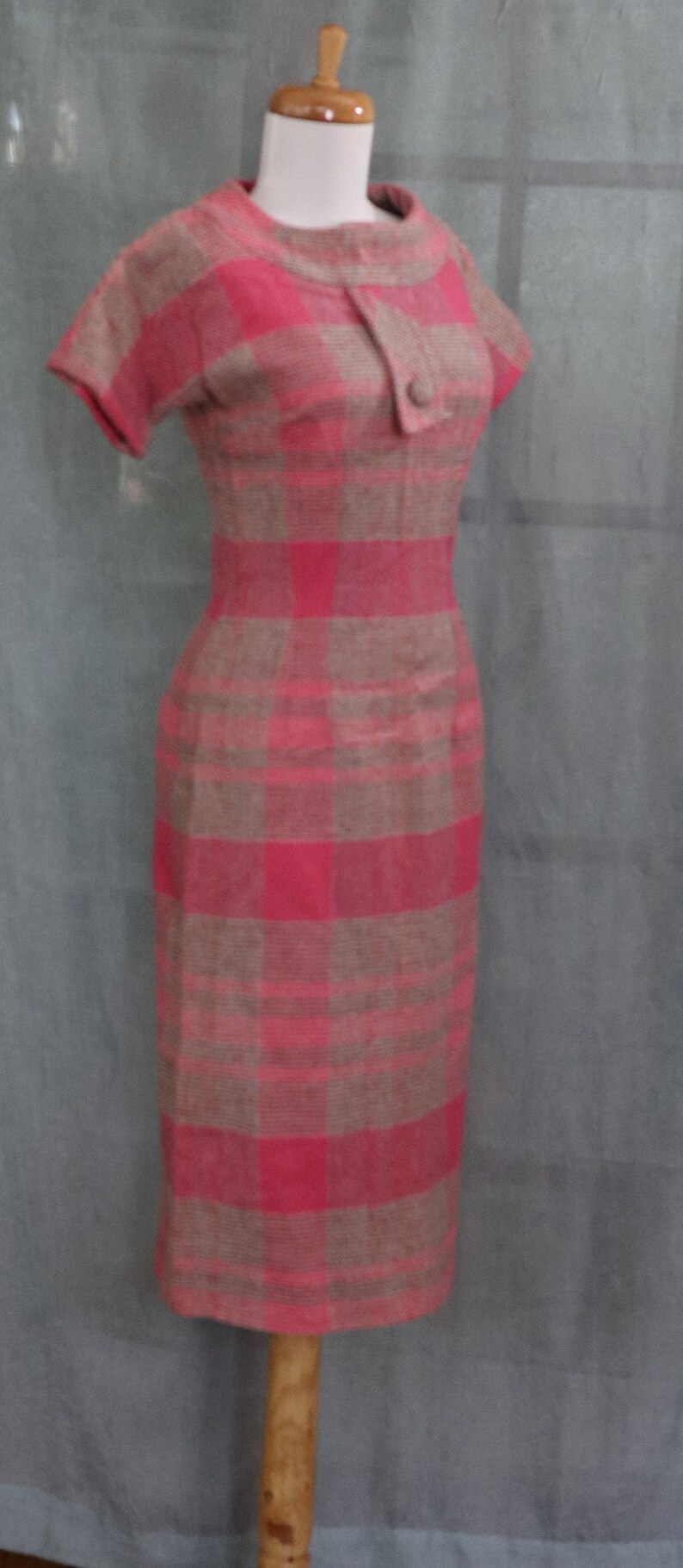 May include: A pink and brown plaid dress with short sleeves and a button closure at the neckline. The dress is on a mannequin.