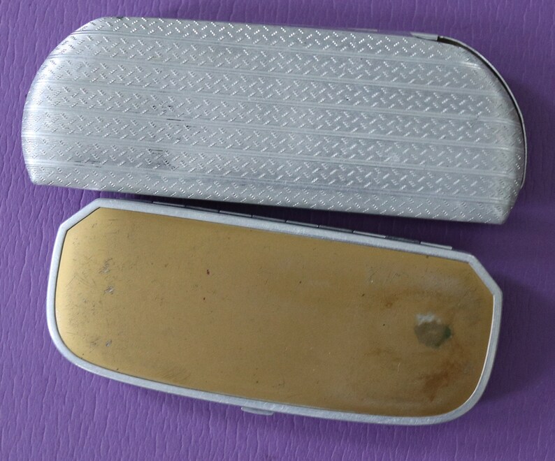 May include: Two vintage eyeglass cases. The top case is silver with a diamond pattern. The bottom case is gold with a worn surface.