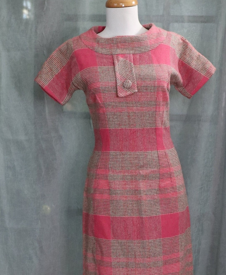 May include: A pink and brown plaid dress with a short sleeve and a round neckline. The dress has a button closure at the neck.
