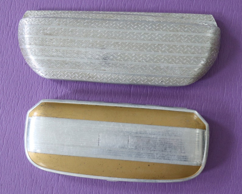 May include: Two vintage metal eyeglass cases. The top case is silver with a textured pattern. The bottom case is gold with a silver band.