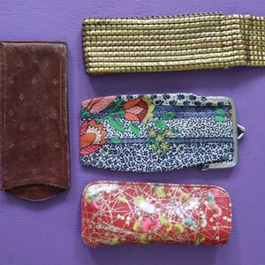 May include: Four different vintage style purses or wallets. One is a brown leather wallet with a floral pattern. Another is a gold mesh wallet. The third is a blue and white floral fabric wallet with a silver clasp. The last is a red and gold fabric wallet with a floral pattern.