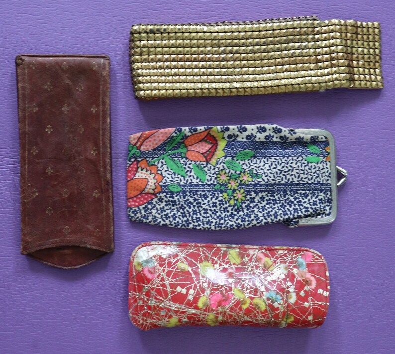 May include: Four different vintage style purses or wallets. One is a brown leather wallet with a floral pattern. Another is a gold mesh wallet. The third is a blue and white floral fabric wallet with a silver clasp. The last is a red and gold fabric wallet with a floral pattern.
