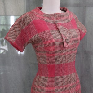 May include: A pink and brown plaid dress with a short sleeve and a button closure at the neck.