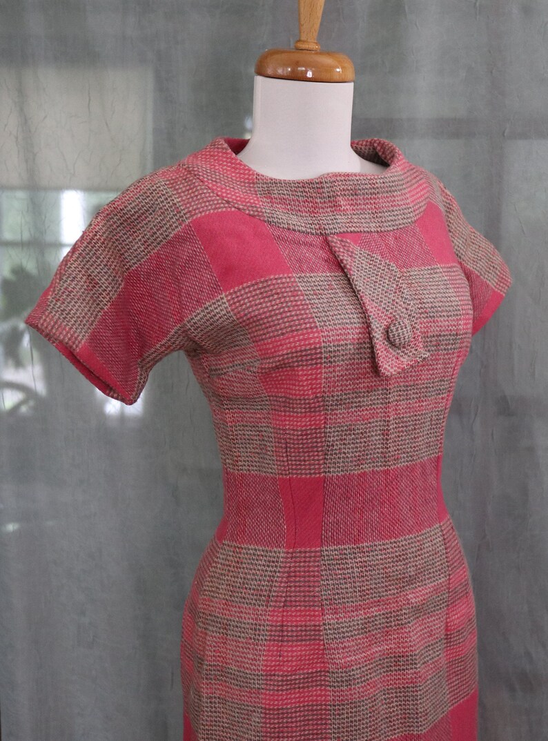 May include: A pink and brown plaid dress with a short sleeve and a button closure at the neck.