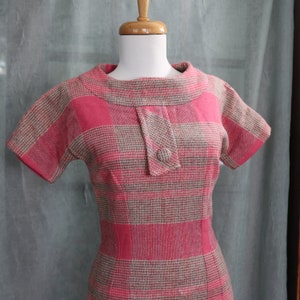 May include: A pink and brown plaid dress with a short sleeve and a button closure at the neck.
